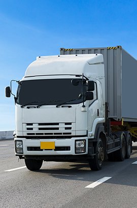 A white semi-truck with a cargo container driving on a highway under a clear blue sky.
